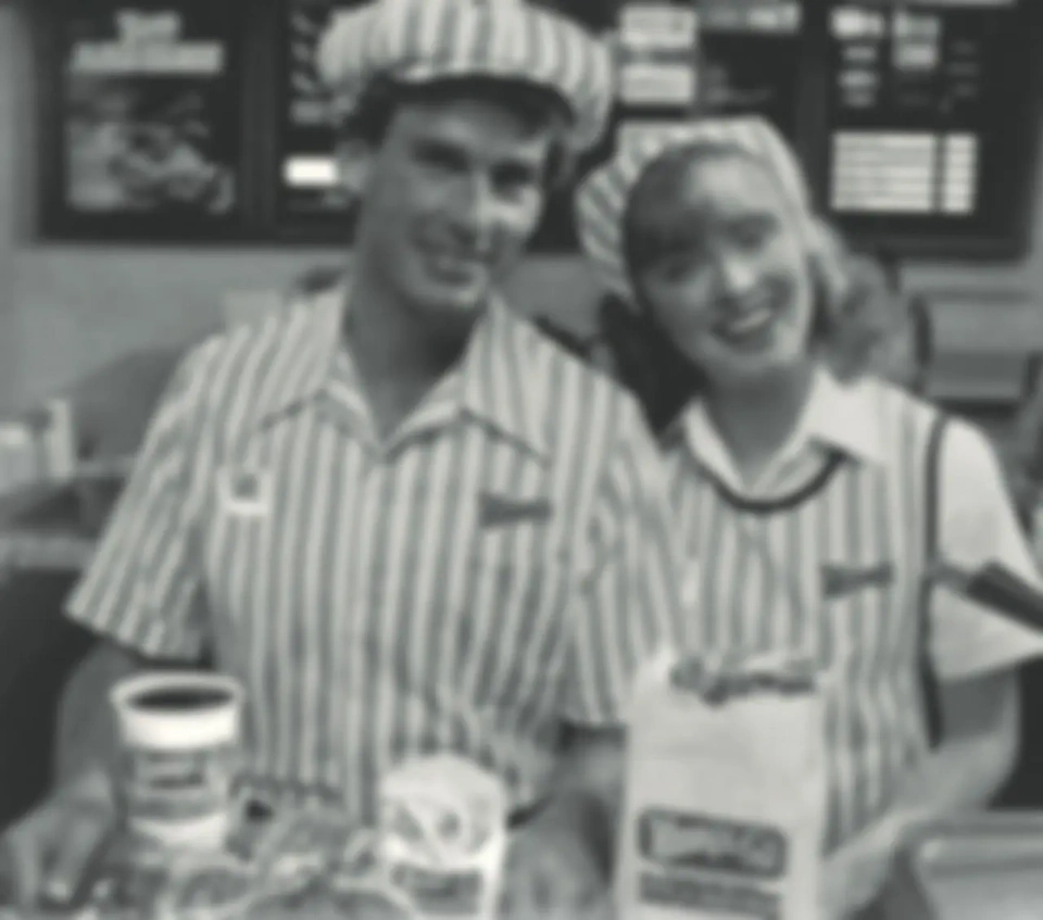 Heavily blurred black-and-white photograph of two uniformed workers behind a counter, before restoration